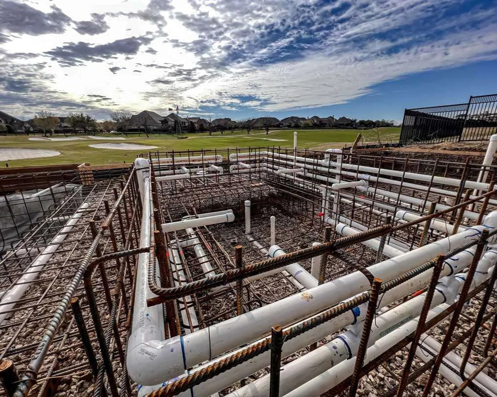 Swimming pool Construction site with concrete foundation and metal rebar under a blue sky.