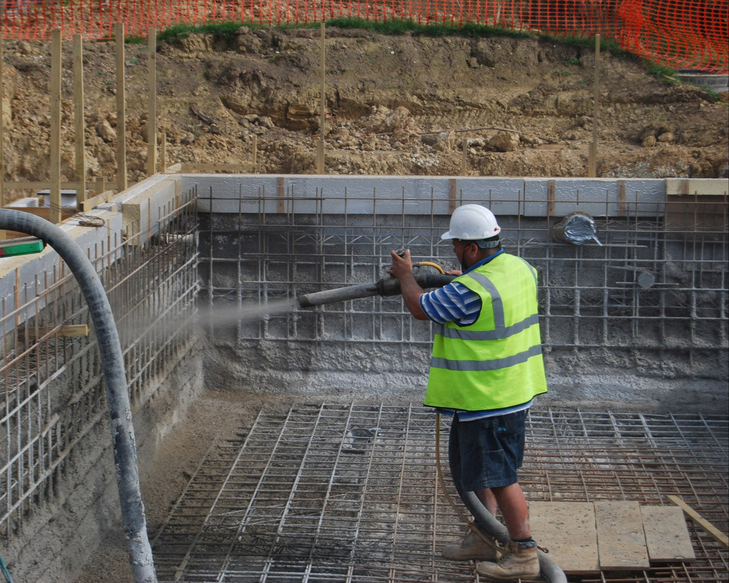Worker in a construction site using a hose, wearing a safety vest and helmet.