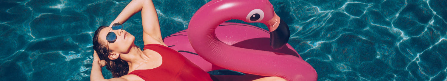 Woman lounging on a pink flamingo pool float in clear blue water