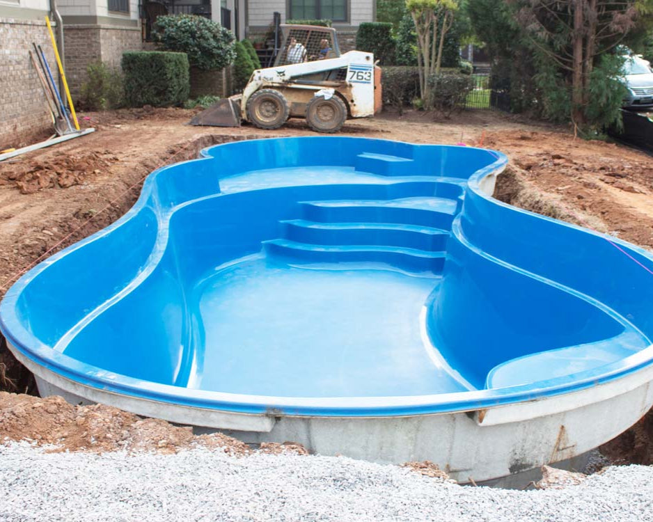 Blue FRP pool being installed in a backyard with construction equipment.