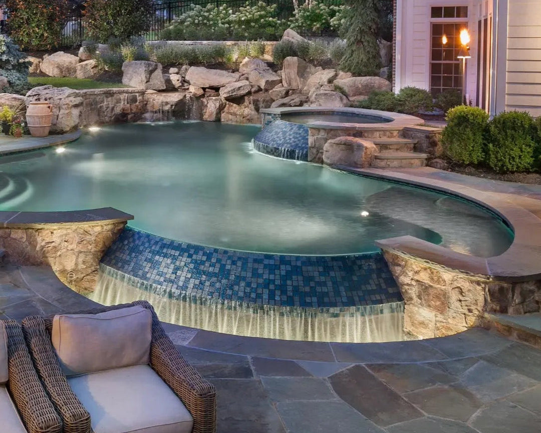 Luxury pool with lounge chairs, rocks, and garden lights at night.