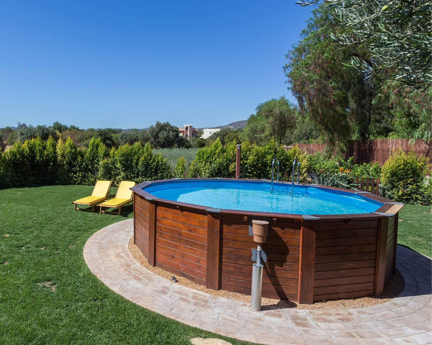 Wooden above-ground pool in a backyard with green grass and trees.