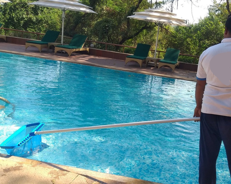 Person cleaning a pool with green chairs and umbrellas in the background