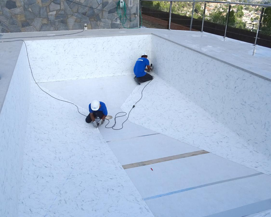 Two workers applying waterproofing material to a pool deck with a scenic background.