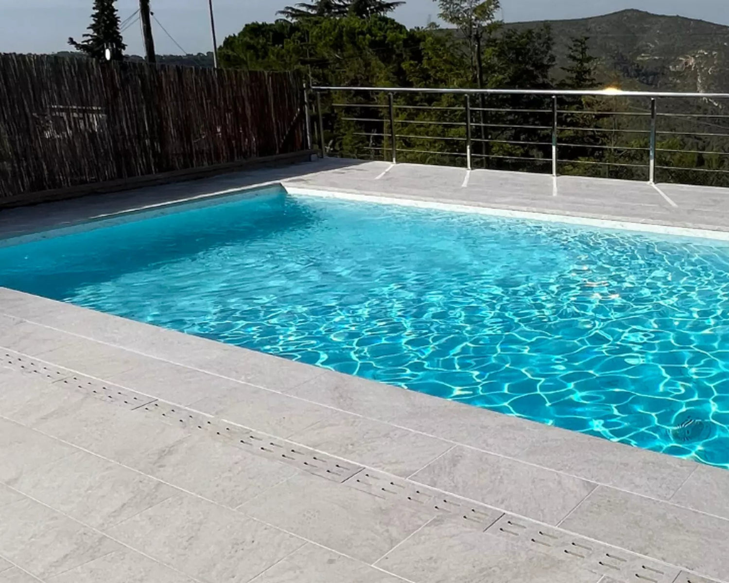 Rectangular pool with clear blue water, surrounded by a wooden fence and greenery.